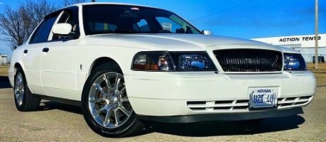 2000 Mercury Grand Marquis - A white 2000 Mercury Grand Marquis is shown from a low angle, highlighting its front end and custom wheels.