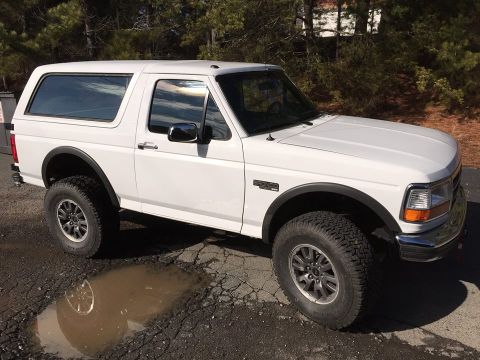 1988 Ford Bronco - This white Ford Bronco is parked on a rough surface with a puddle reflecting its tire.
