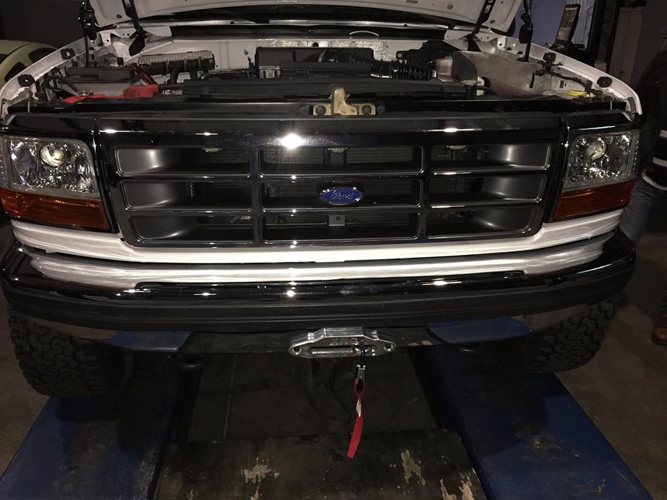 White Ford truck front end with chrome grille and headlights, hood open, winch mounted on bumper