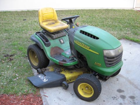 2006 Honda RANCHER - John Deere L120 riding mower parked on concrete with grass and mulch nearby.