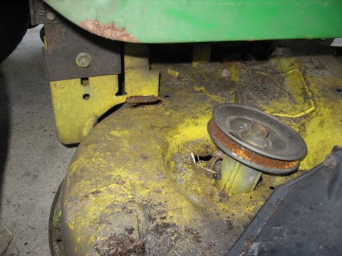 2006 Honda RANCHER - The underside of a lawn mower deck shows a pulley system with signs of wear and rust.