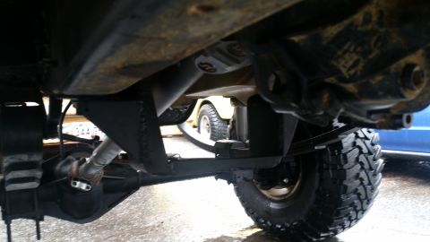 1988 Ford Bronco - Focus on the undercarriage components, including the leaf springs and driveshaft, with another vehicle partially visible.