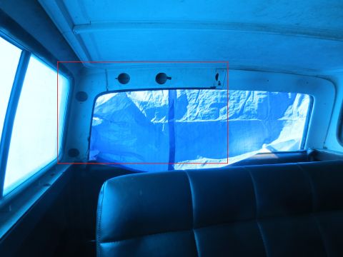 1978 Ford Bronco - The rear window of a vehicle is covered with a blue tarp, obscuring the view outside.