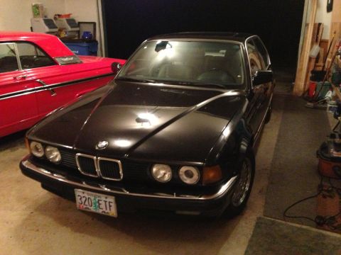 1988 BMW 7 Series - A black BMW sedan is parked in a garage, with a red classic car visible to its left.