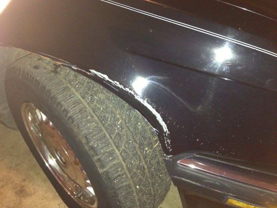 Black car fender with scraped paint and rust near the tire