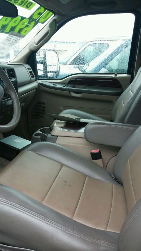 2003 Ford Excursion - Interior view of a 2003 Ford Excursion, showing tan leather seats and the dashboard. Other vehicles are visible through the windows.