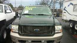 2003 Ford Excursion - Front view of a dark green 2003 Ford Excursion, parked outdoors with other vehicles and a trailer nearby.