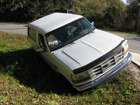 1994 Ford Bronco - A white 1994 Ford Bronco is parked on the side of a road, with another vehicle visible in the background.