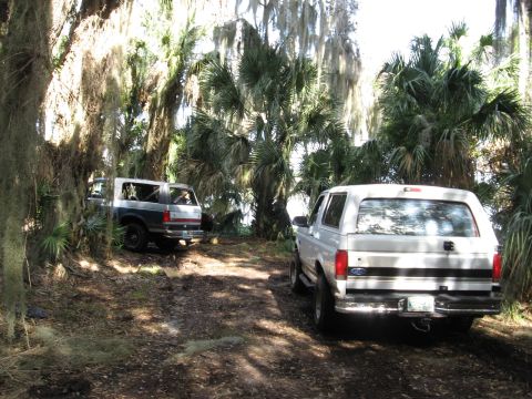 1994 Ford Bronco - Two Ford Broncos navigate a wooded trail, with one vehicle in the foreground and another further down the path.