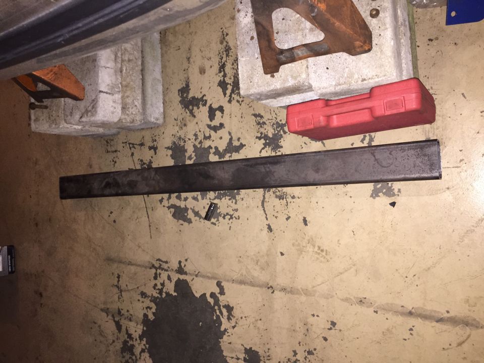 Metal bar, red toolbox, and jack stands on a dirty garage floor