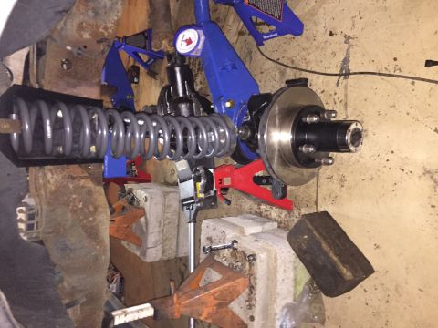 1994 Ford Bronco - Front suspension and brake assembly, including a coil spring, is supported by jack stands in a workshop setting.