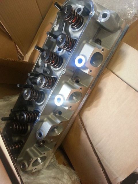 1979 Ford Bronco - An engine cylinder head with valves and springs is shown, partially obscured by cardboard packaging.