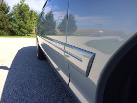 2003 Ford Crown Victoria - Close-up of a car's side panel and trim, with reflections of the sky and trees in the polished surface.