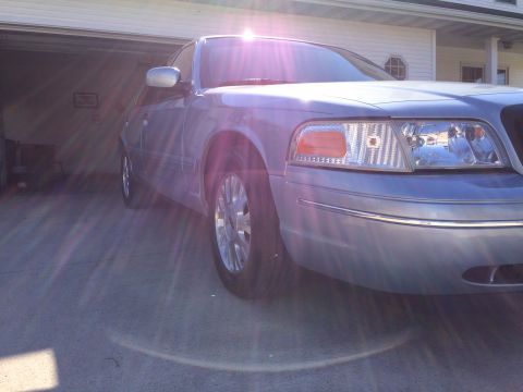 2003 Ford Crown Victoria - A blue 2003 Ford Crown Victoria is parked in front of a garage, with sunlight glinting off the windshield.