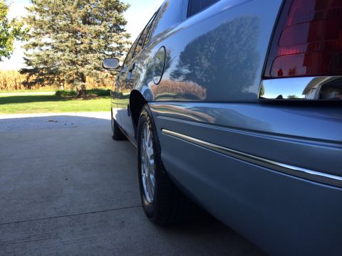 2003 Ford Crown Victoria - Rear quarter panel view of a light blue sedan, likely a 2003 Ford Crown Victoria, showing chrome trim and the taillight assembly.