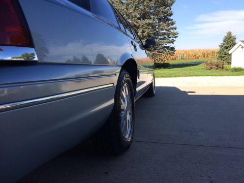 2003 Ford Crown Victoria - A silver 2003 Ford Crown Victoria is parked outside a house with a cornfield in the background.