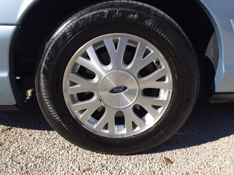 2003 Ford Crown Victoria - This image shows a close-up of a silver wheel with a Ford logo, part of a light blue vehicle.