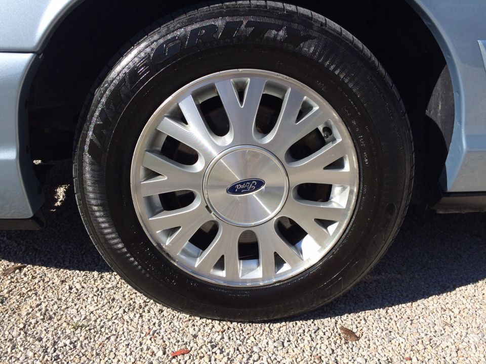 Close-up of a silver Ford wheel with a blue Ford logo on a light blue car