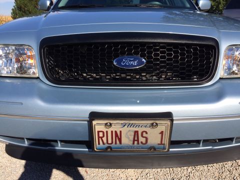 2003 Ford Crown Victoria - Front view of a light blue 2003 Ford Crown Victoria, its distinctive honeycomb grille and a personalized Illinois license plate.