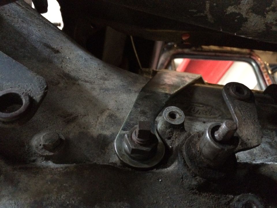 Close-up of transmission linkage with a Ford logo visible on the casing. A red interior is visible in the background