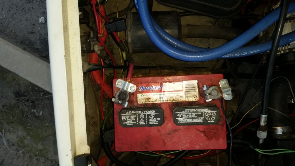 Red Duracell battery in a vehicle engine bay with blue hoses and red wiring