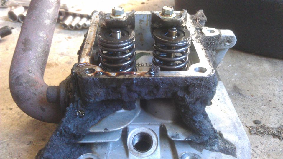 Engine cylinder head with visible valves and springs, covered in grime