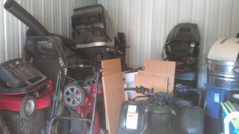 Green four-wheeler in storage unit with lawnmowers and engines
