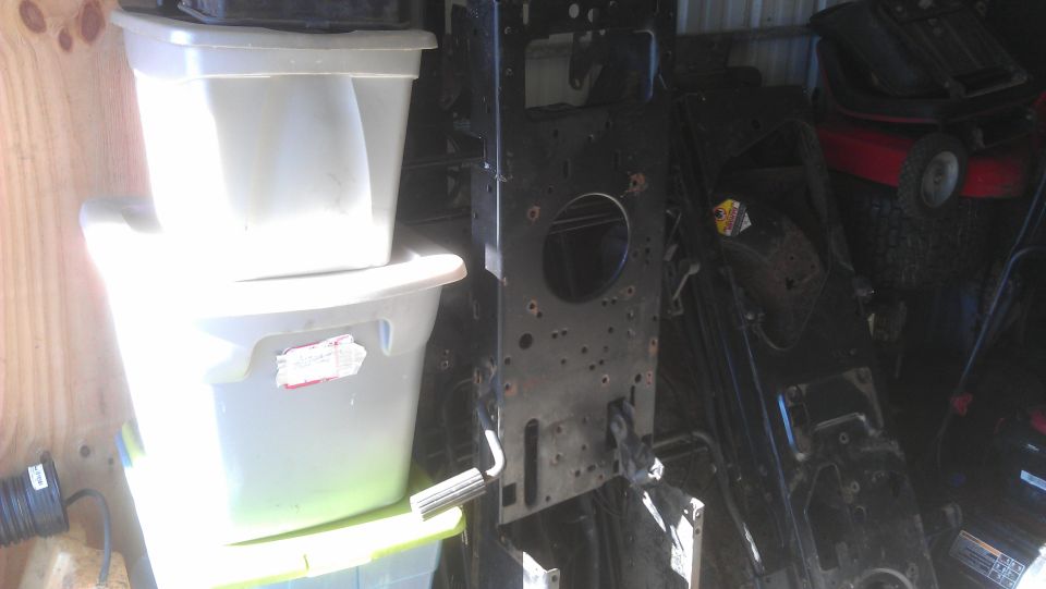 Stripped riding mower steel frame stood on end in shed beside stacked plastic totes
