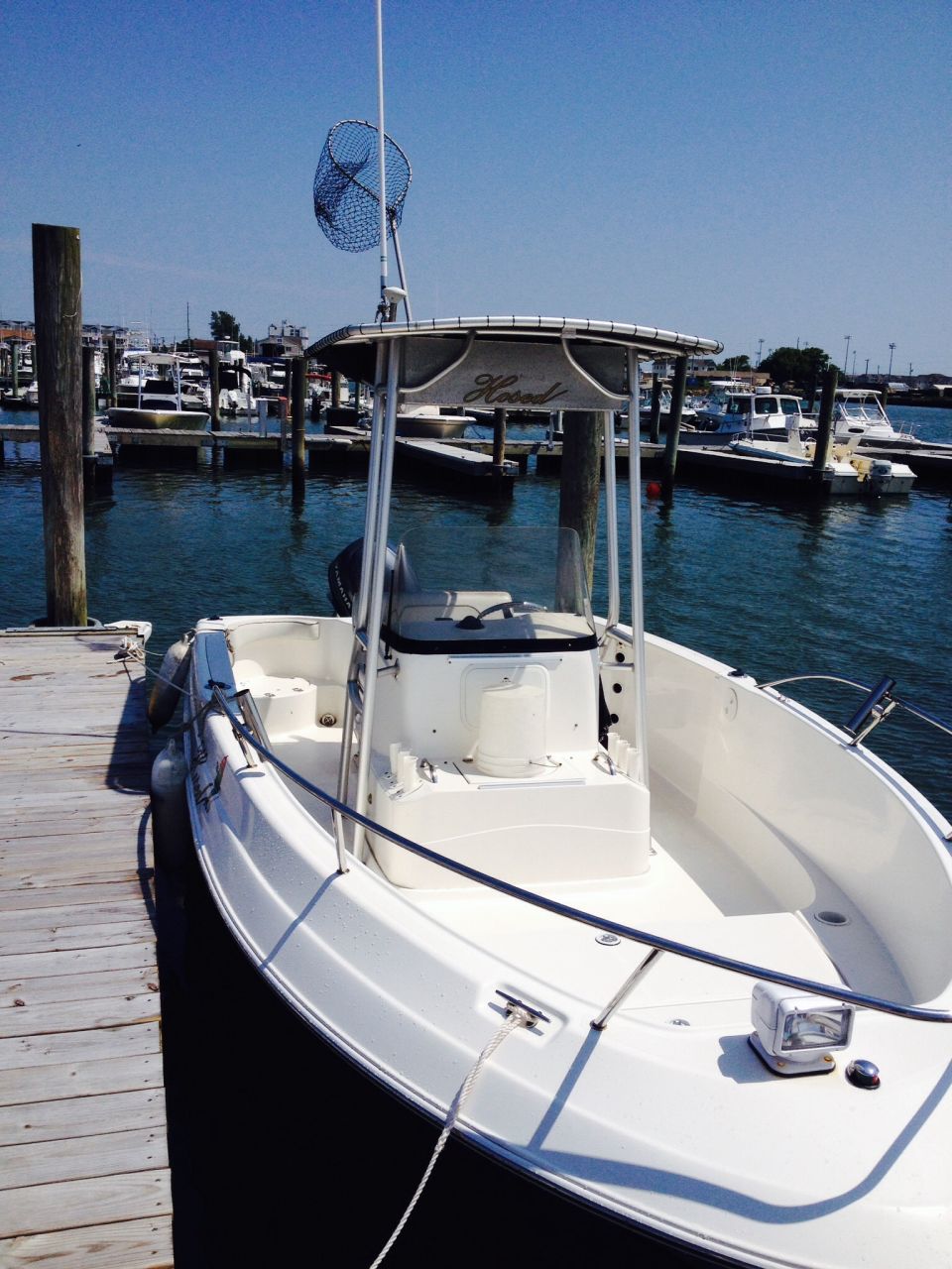 White boat docked at a wooden pier, with a fishing net mounted on a pole