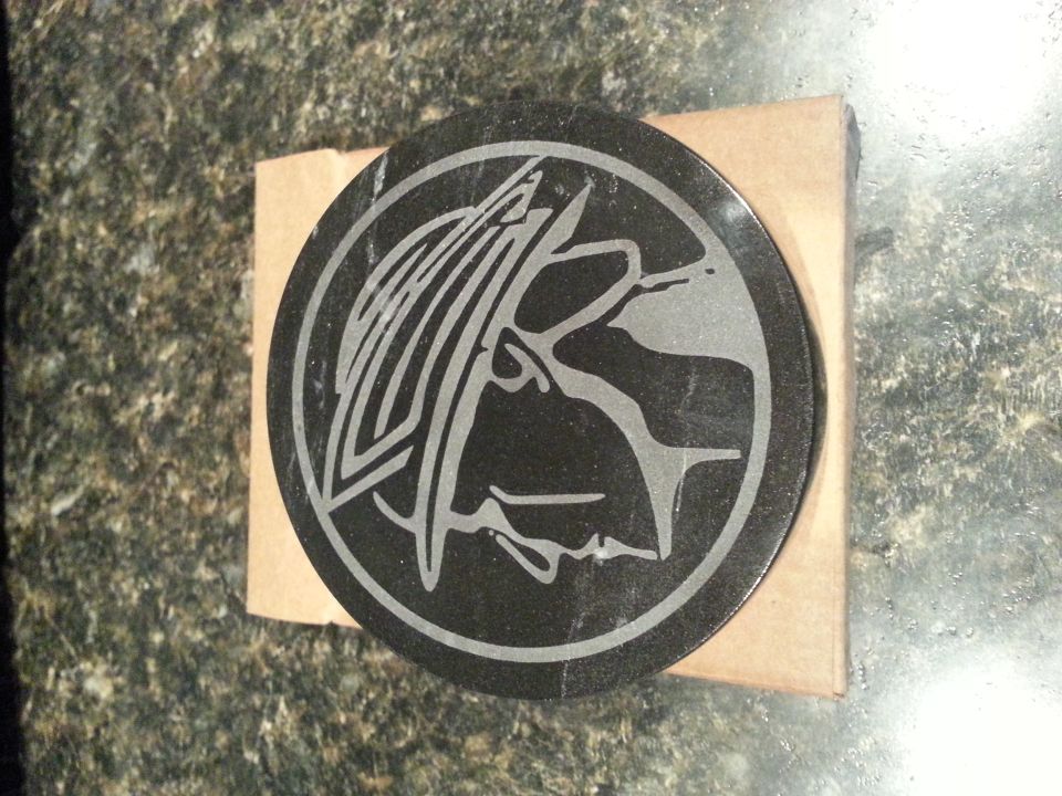 Round black emblem with a stylized bird or animal design etched in silver