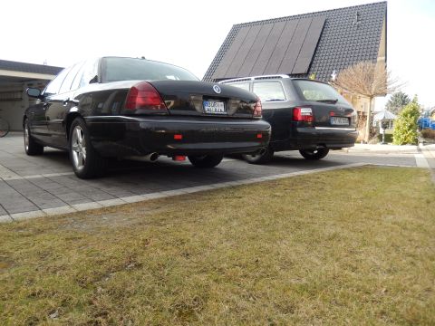 2003 Mercury Marauder - Two sedans, including a 2003 Mercury Marauder, are parked on a paved driveway in front of a house.