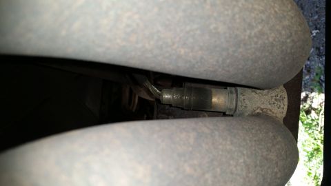 1991 Ford F-250 - A close-up view of an oxygen sensor mounted on a vehicle's exhaust system, nestled between two large pipes.