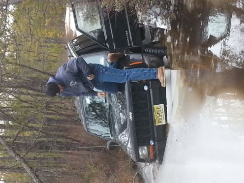 1987 Toyota 4Runner - A black Jeep Cherokee is partially submerged in muddy water, with its driver's door open.