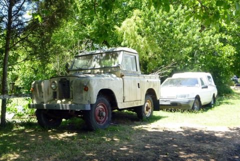 1969 Lincoln Continental - Two vehicles, a Land Rover pickup and a sedan, sit parked outdoors amongst trees and grass.