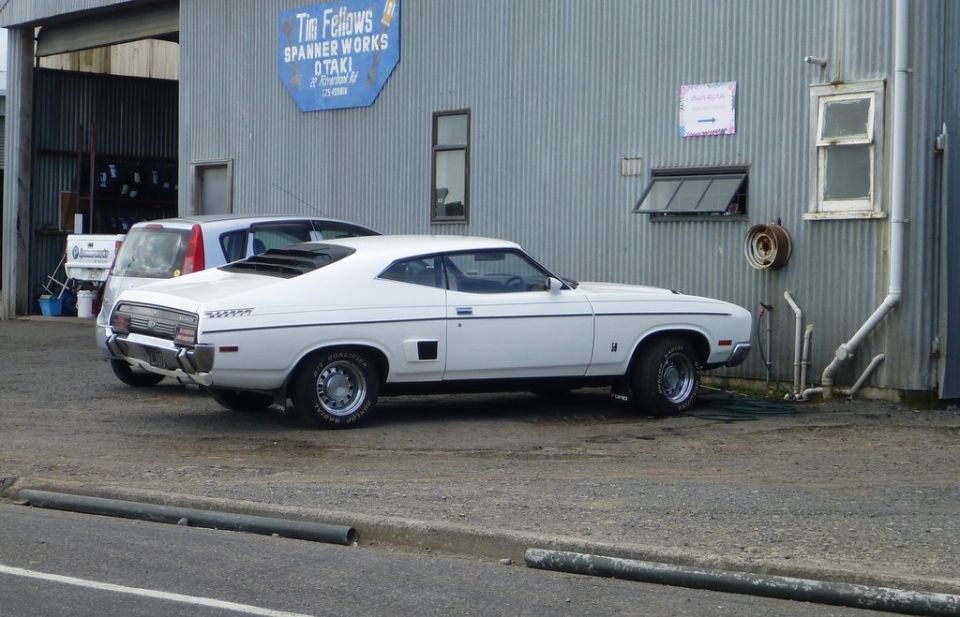 White coupe with louvred rear window and side vents parked next to a silver hatchback