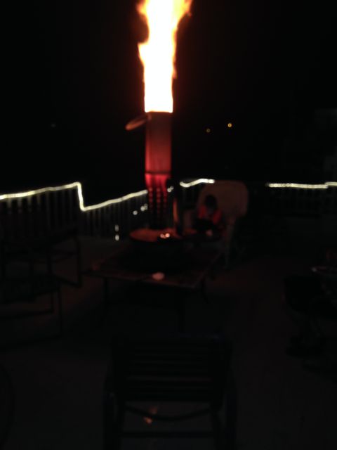 1961 International Scout 800 - A fire pit burns brightly on a deck at night, with chairs and railings visible in the dim light.