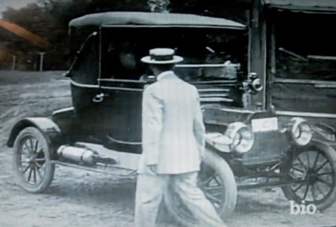 1915 Ford Model T - A man in a suit and hat approaches a dark-colored 1915 Ford Model T, captured in a vintage photograph.