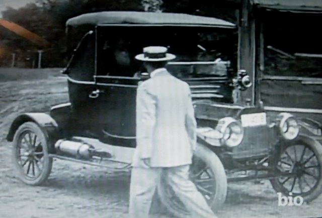 1915 Ford Model T, 3q-front view, dark color, man in suit approaching