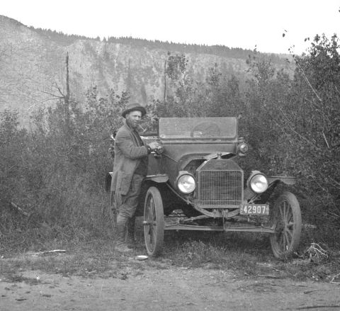 1915 Ford Model T - A man poses with his 1915 Ford Model T, identifiable by its distinctive grille and license plate.