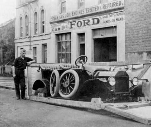 1915 Ford Model T - A 1915 Ford Model T is loaded onto a trailer outside a Ford service building that advertises repairs and parts.
