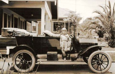 1915 Ford Model T - A child poses with a vintage automobile parked in front of a residential building.