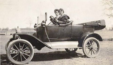 1915 Ford Model T - A vintage 1915 Ford Model T touring car is captured from the side, with two individuals seated inside.