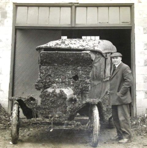 1915 Ford Model T - Man stands next to a heavily mud-caked 1915 Ford Model T, likely after an off-road excursion.