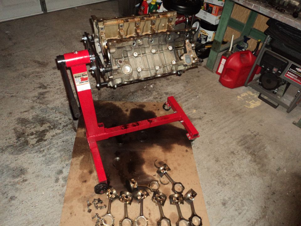 Engine block on a red stand with pistons and connecting rods laid out on cardboard