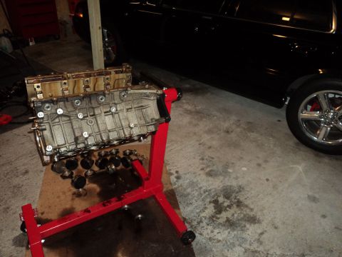2004 Mercury Grand Marquis - An engine block is displayed on a red engine stand in a garage setting, with a black vehicle partially visible in the background.
