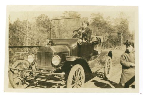 1915 Ford Model T - A vintage touring car with a driver and passenger poses outdoors on a dirt road.