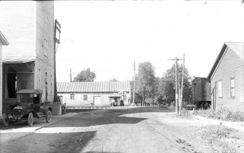 1915 Ford Model T - A vintage Ford Model T is parked on a dirt road next to a building, with a train car visible in the background.