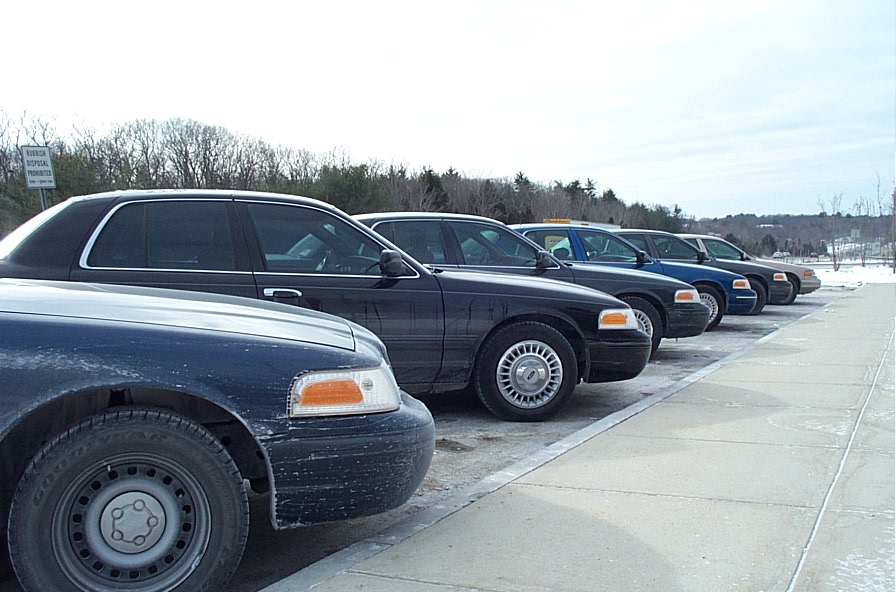 Side view of a line of dark 1991 Ford Crown Victoria LTD sedans parked in a lot
