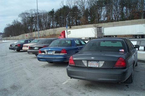 1991 Ford LTD Crown Victoria - Several Ford Crown Victoria police sedans are parked in a lot, with a semi-trailer truck in the background.