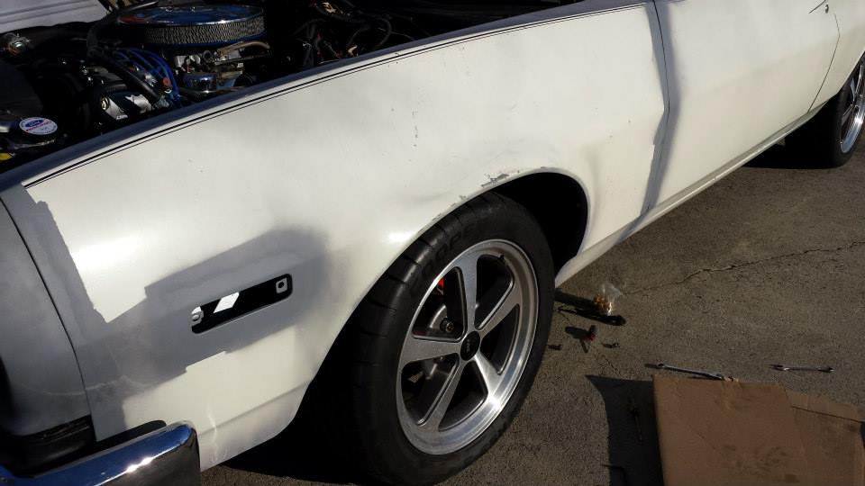 White coupe, hood up showing engine. Side view of front fender and wheel